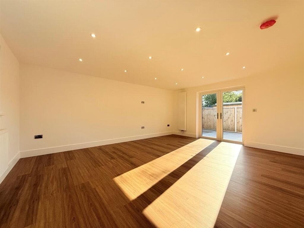 Dark oak LVT plank flooring in a large empty room, sunlight streaming through French doors onto a patio