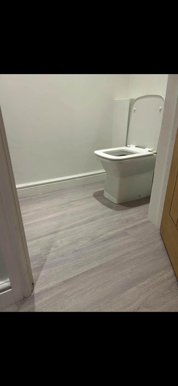 Grey oak-effect sheet vinyl fitted in a washroom cubicle, sealed neatly to the skirting