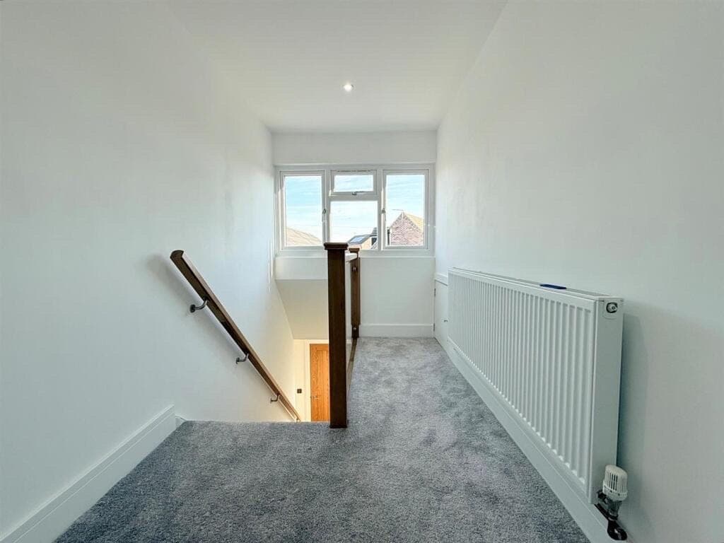 Grey twist pile carpet fitted to a landing and down the stairs, beside an oak handrail and newel post