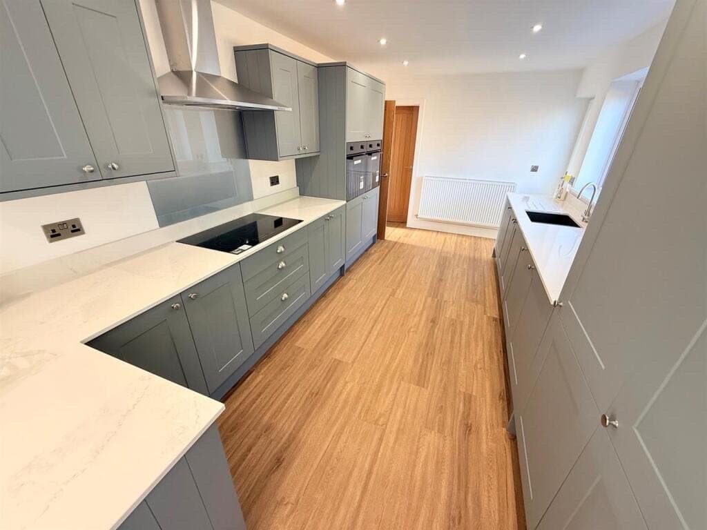 Honey oak LVT plank flooring in a galley kitchen with sage green shaker units and white quartz worktops