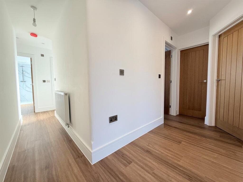 Warm oak LVT plank flooring running the length of a hallway lined with oak doors, with a shower room at the far end