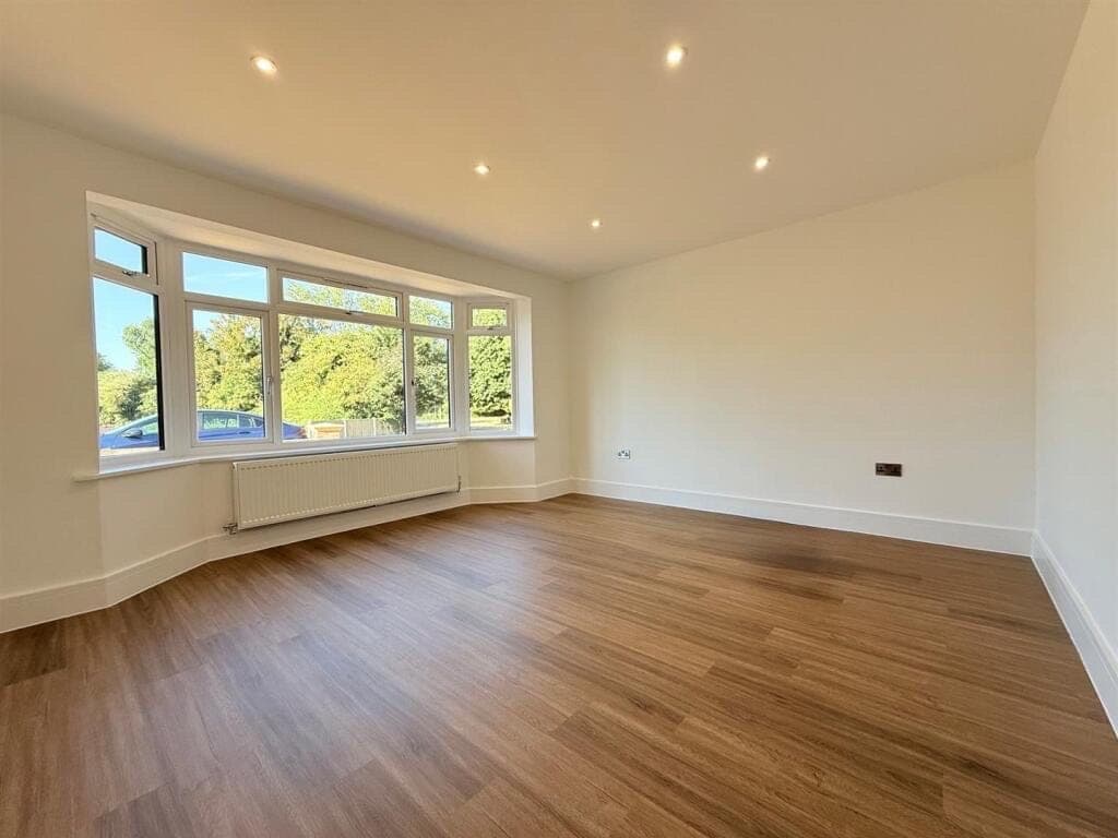 Mid-brown oak LVT plank flooring in an empty living room with a curved bay window overlooking trees