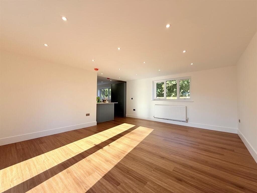 Warm oak LVT flooring across an open-plan living room, sunlight falling in stripes towards a kitchen island beyond