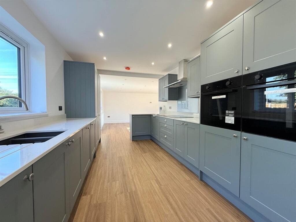Honey oak LVT flooring in a shaker kitchen diner with sage green cabinetry, double ovens and quartz worktops