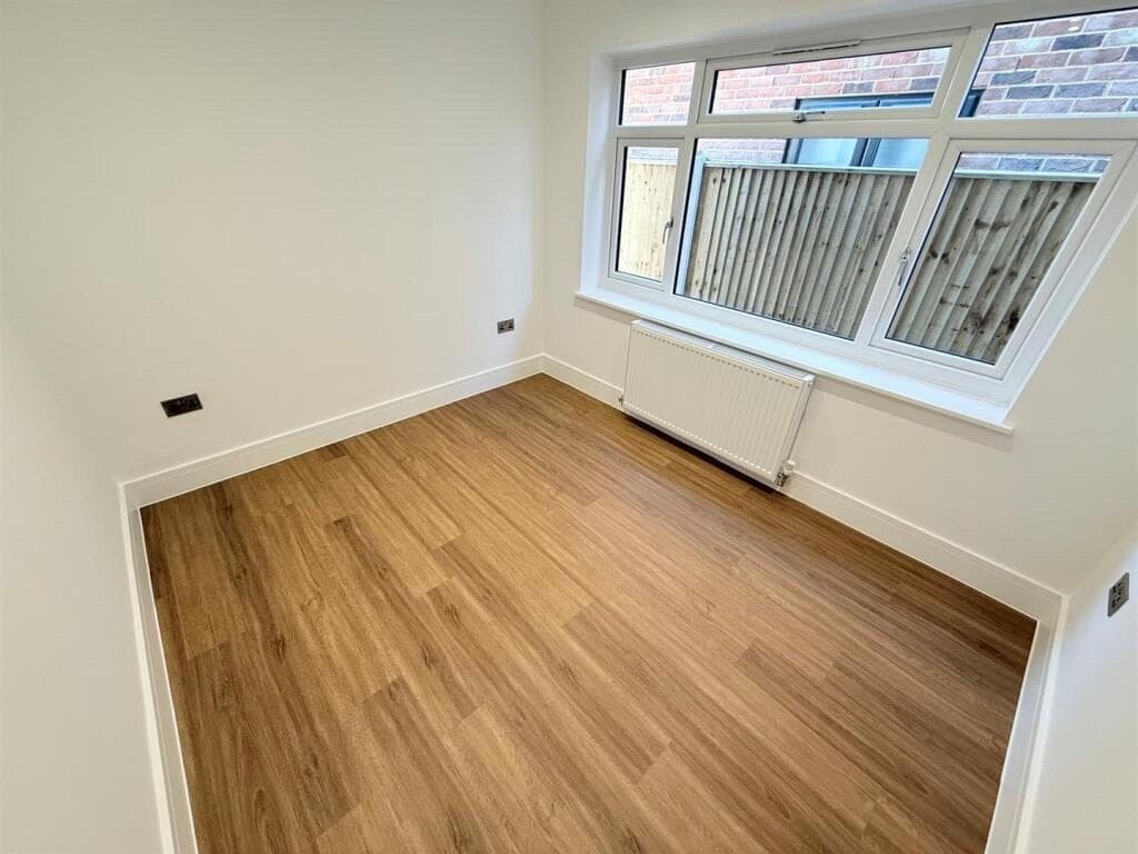 Honey oak LVT plank flooring in a small bedroom with a window looking onto a fenced garden