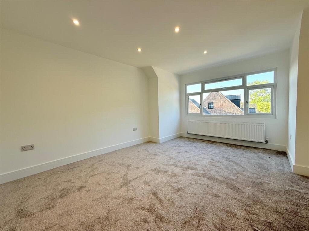 Oatmeal twist pile carpet freshly fitted in an empty bedroom with a window and white column radiator