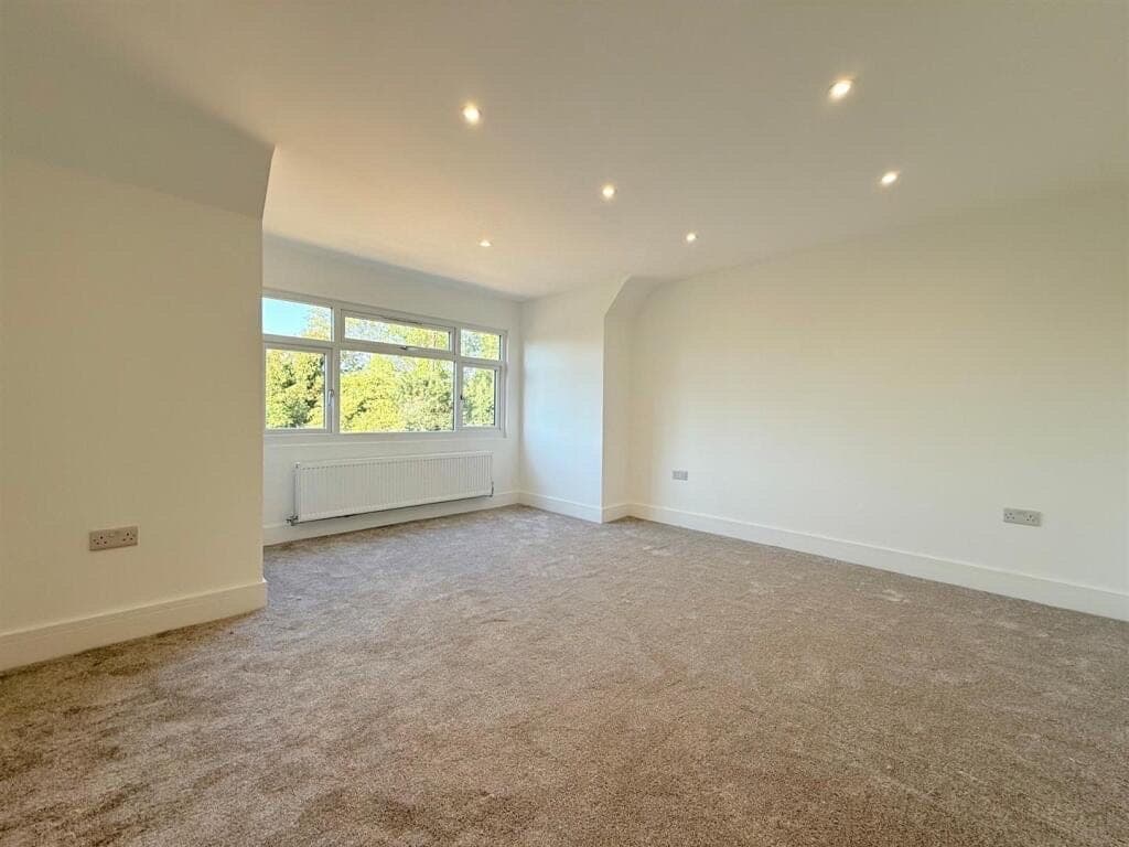 Oatmeal twist pile carpet fitted in a dormer bedroom with a sloped ceiling and a window onto trees