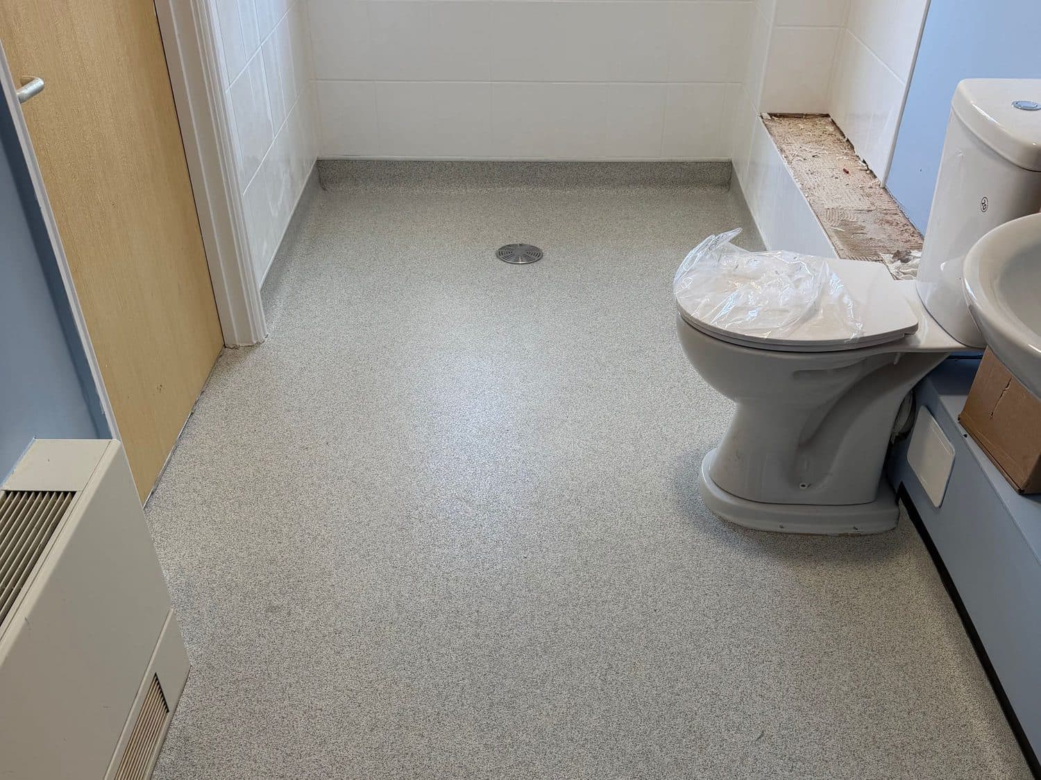 Slip-resistant safety vinyl wet room floor laid to fall towards a centre gully, coved up to the tiled walls and finished level-access through the doorway