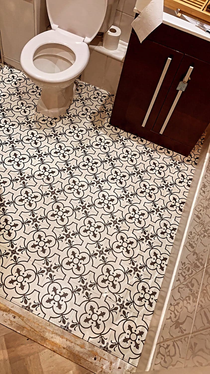 Monochrome Victorian tile-effect sheet vinyl fitted in a cloakroom, cut around the toilet pedestal and running to the doorway where it meets parquet flooring