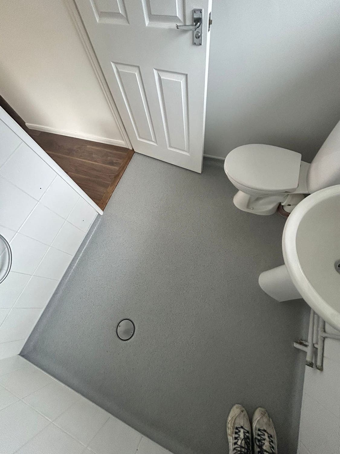 Grey speckled safety vinyl wet room floor with a sealed flush drain, running level-access through the doorway to meet dark wood-effect flooring