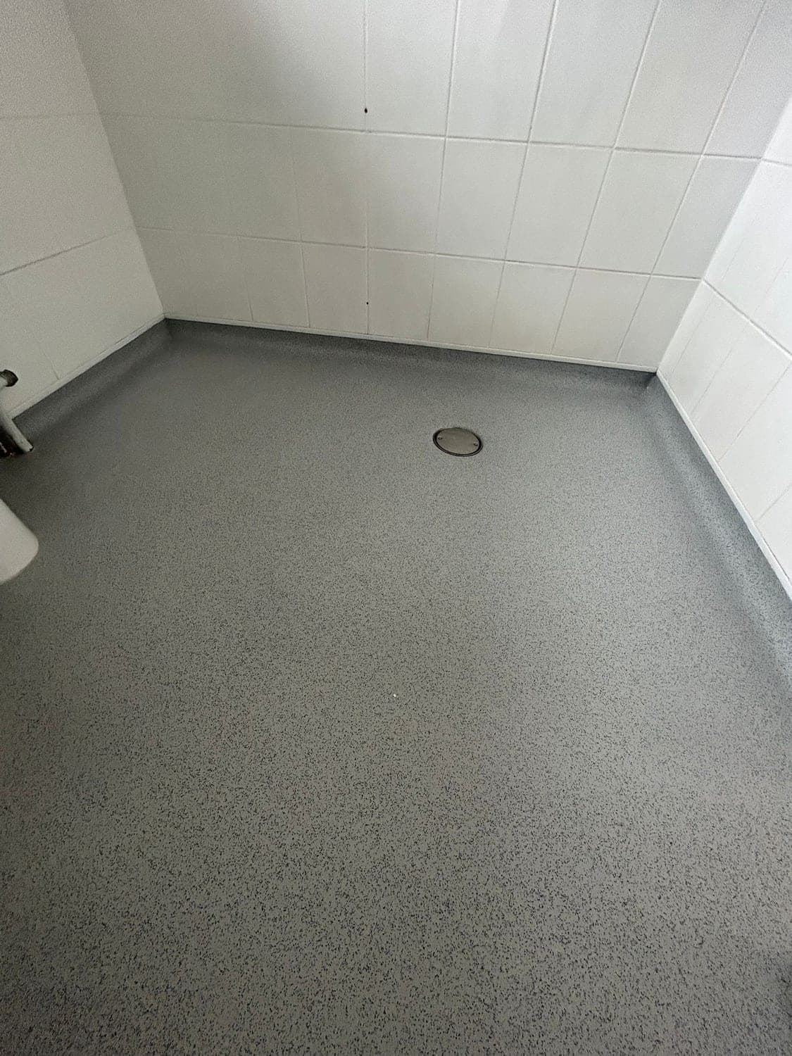 Close view of a welded safety vinyl wet room floor coved up to white tiled walls, laid to fall towards a clamped centre drain