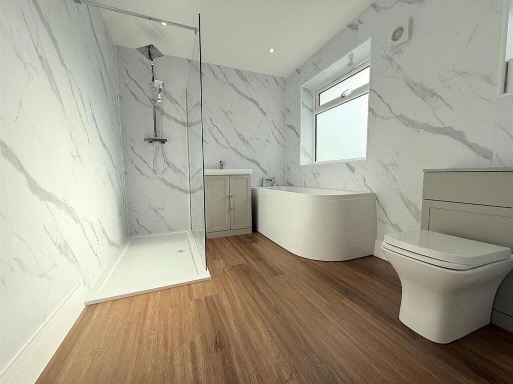 Warm oak wood-effect vinyl flooring in a bathroom with a walk-in shower, corner bath and marble-effect wall panels